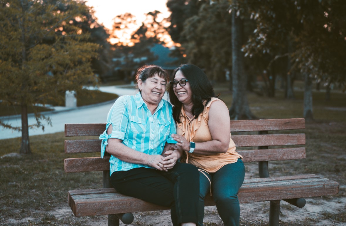 Two women sitting closely on a bench laughing together