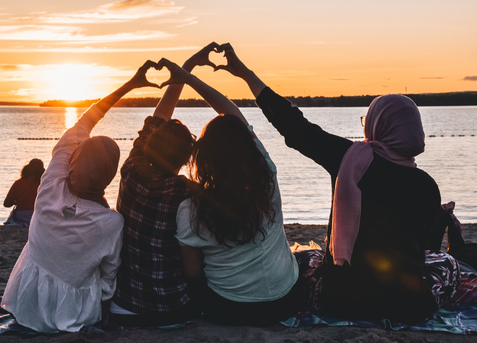 Group of people sitting at the beach connecting their hands to make heart symbols